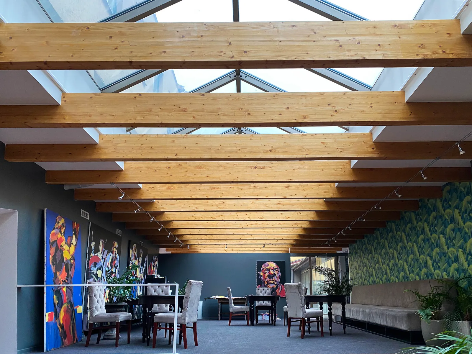Erdvė po stiklo stogu su medinėmis sijomis ir paveikslais